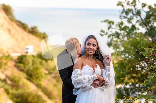 Image of Newlyweds hug against the backdrop of a beautiful landscape, the guy kisses the shoulder of the girl who shyly looks up