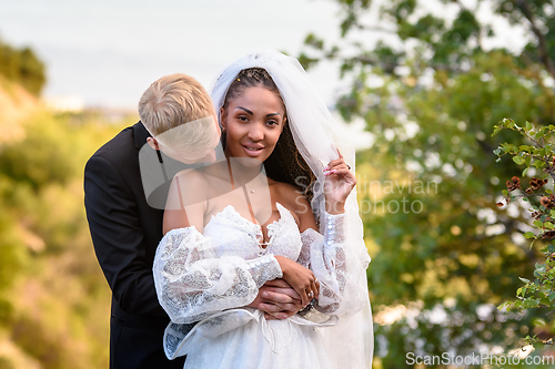 Image of Newlyweds hug against the backdrop of a beautiful landscape, the guy kisses the neck of the girl who is looking into the frame