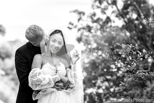 Image of Happy newlyweds hug against the backdrop of a beautiful mountain landscape, the guy kisses the girl, the girl looks into the frame, black and white version