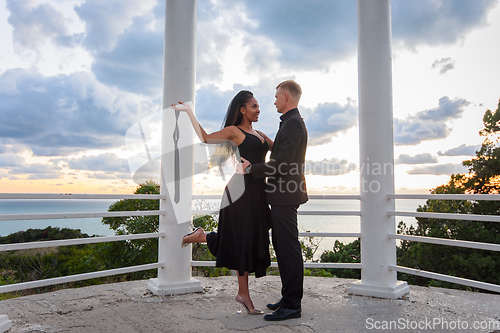 Image of A young couple in a gazebo against the backdrop of a beautiful landscape, the girl holds the guy's tie