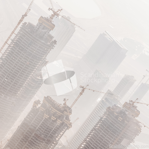 Image of Skyscrappers construction site with cranes on top of buildings.