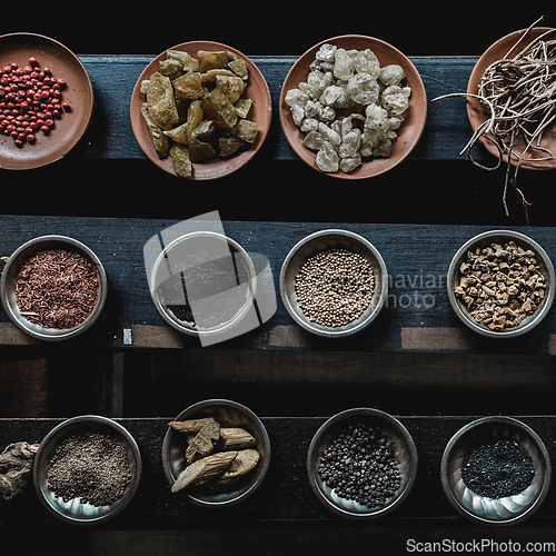 Image of Various spices displaied on small ceramic and metal plates on black wooden background.