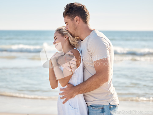 Image of Beach, happy and couple hugging with love, care and romance while on a honeymoon vacation. Happiness, kiss and loving man embracing his wife from behind by the ocean on a seaside holiday in Maldives.