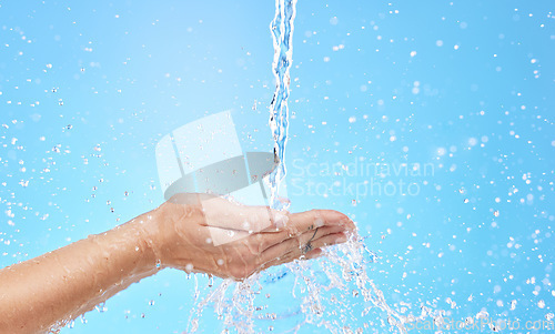 Image of Hand, water and cleaning with a splash in studio on a blue background for hygiene or hydration. Mockup, health and wellness with a female washing under a water splash in the bathroom for skincare