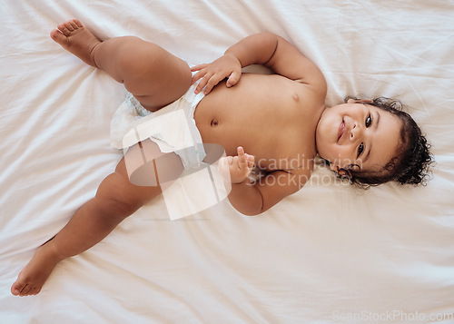 Image of Happy baby, smile and relax on bed in family home bedroom for diaper change, bedtime or healthy childcare. Child, happiness and body care in disposable nappy or kids portrait from above in nursery