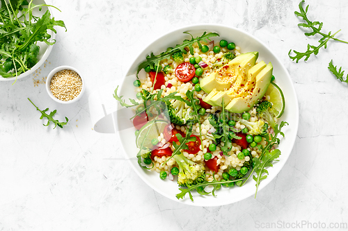 Image of Couscous salad with broccoli, green peas, tomatoes, avocado and fresh arugula. Healthy natural plant based vegetarian food for lunch, israeli cuisine, top view