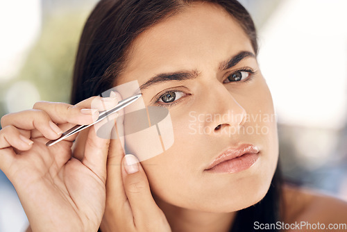 Image of Woman in mirror plucking eyebrows with tweezers and grooming facial routine in morning. Beauty, skincare and tweezing eyebrow hair, portrait of Indian woman face in reflection in bathroom treatment.