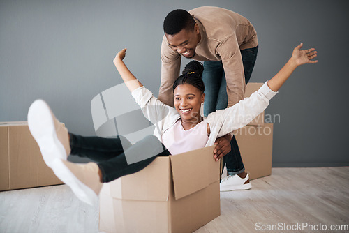 Image of Couple, box and moving into real estate, home and fun while unpacking, playing and bond in a living room. House, fun and man with woman on a floor playful, laughing and celebrating their dream home