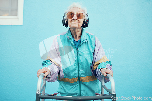 Image of City, fashion and senior woman with headphones listening to music, audio and radio on blue background wall. Freedom, style and elderly female with modern, urban and trendy clothes with walker in town