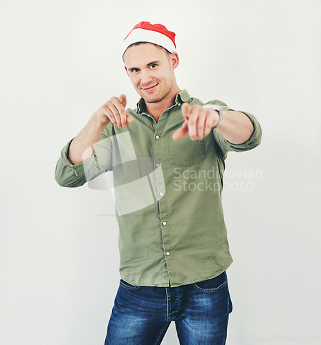 Image of Christmas, portrait and festive with a model man in studio on a gray background wearing a hat for the holidays. Tradition, celebration and seasons greetings with a male in a santa cap while pointing