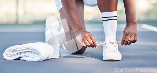 Image of Tennis, athlete and sports feet tying her shoe laces ready for game, competition or training outdoor with water bottle gear. Fitness sneakers of black woman foot on ground zoom in workout motivation