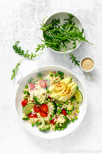 Image of Couscous salad with broccoli, green peas, tomatoes, avocado and fresh arugula. Healthy natural plant based vegetarian food for lunch, israeli cuisine, top view