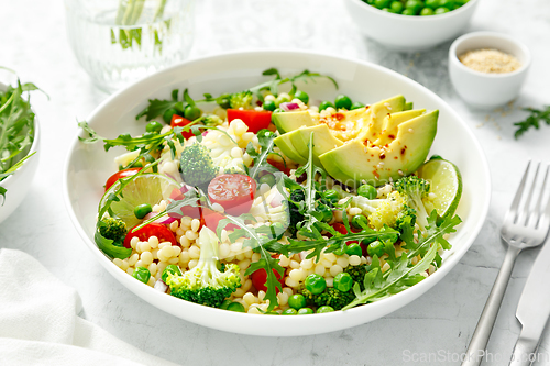 Image of Couscous salad with broccoli, green peas, tomatoes, avocado and fresh arugula. Healthy natural plant based vegetarian food for lunch, israeli cuisine