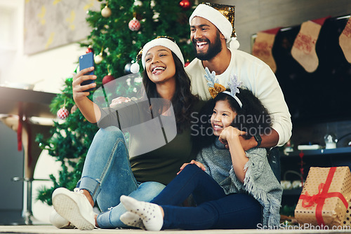 Image of Selfie, family and christmas with a mother, father and daughter sitting for a photograph at home with a gift by a tree. Kids, fun and love with a girl, woman and man posing for a festive picture