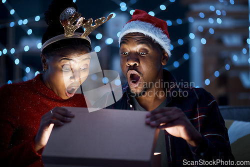 Image of Black couple, box and christmas gift open in surprise, wow and shock by magic light and looking excited. Night, couple and gift box fantasy, omg and amazed while sharing festive holiday in a home