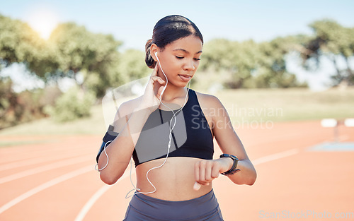 Image of Music, earphones and runner woman pulse check on workout, training and athlete break. Wellness, fitness and running girl pause at stadium track for performance analysis on smartwatch app.