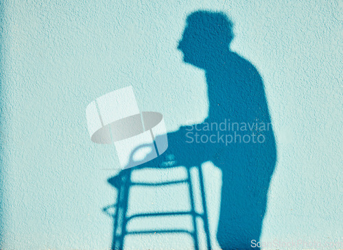 Image of Shadow, disability and walking with a senior woman outdoor on a blue wall background on a sunny summer day. Silhouette, handicap and mobility walker with a mature female outside alone for a walk