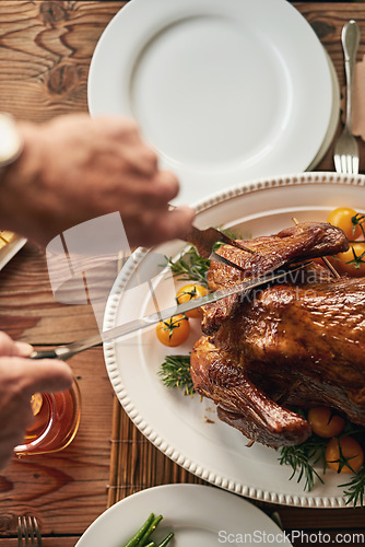 Image of Hands, food and carving the turkey with a senior man using a knife at a dining room table in his home. Chicken, thanksgiving and tradition with a mature male cutting meat during a roast meal or feast