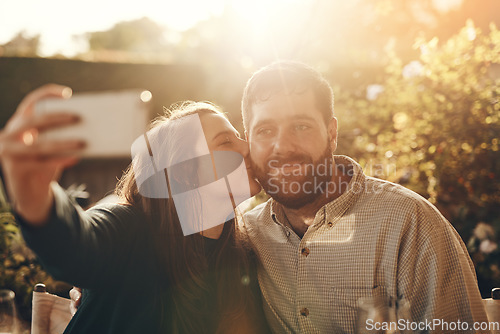 Image of Happy couple, selfie on a phone with a kiss for love, care and support while outdoor in garden with lens flare for summer. Man and woman together with smartphone for social media profile picture