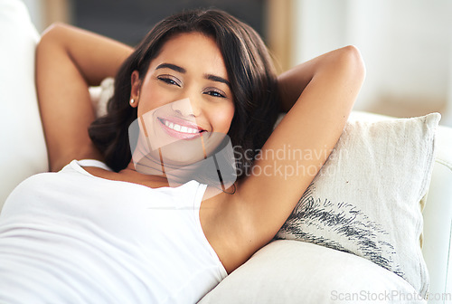 Image of Portrait, relax and happy with a black woman lying on a sofa in the living room of her home over a weekend. Face, smile and rest with a young female chilling in a house with hands behind her head