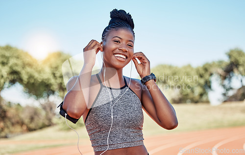 Image of Running, portrait of woman on track with headphones and phone for fitness app on happy workout. Technology, sports and black woman runner with smile streaming music on run for health and wellness.