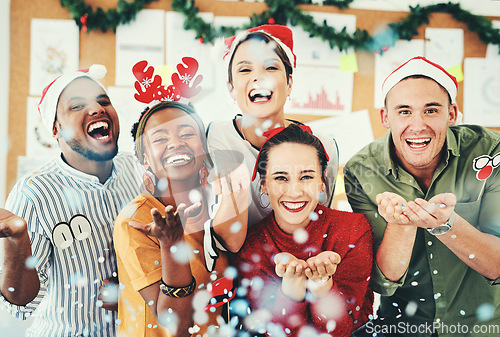 Image of Christmas, office and business people blowing confetti and having fun together. Portrait, xmas party or group of happy employees, workers or coworkers celebrating with paper decorations in workplace