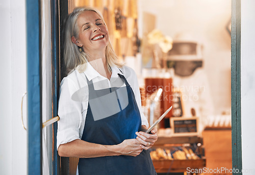 Image of Happy senior business owner with a tablet in her store for startup with technology or mobile device. Leader, entrepreneur and elderly woman standing by an open door to welcome customers in the shop.