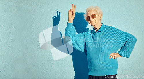 Image of City, fashion and senior woman with peace sign on blue background wall enjoy freedom, weekend and retirement. Energy, hand sign and happy elderly female with cool, modern and trendy clothes in town