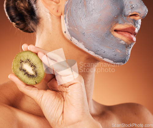 Image of Facial, mask and hand with kiwi for skincare of woman for wellness, beauty and self care routine. Cosmetic, spa and pamper lifestyle girl with natural treatment on brown studio background zoom.