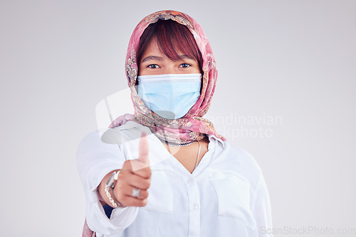 Image of Covid face mask, muslim woman and thumbs up, portrait and vaccine yes vote, safety compliance and emoji, health risk and policy on studio background. Corona virus, thumb up and islamic female hijab