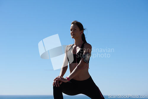 Image of Woman, stretching or earphones or phone armband music in workout, training or exercise in heart health, cardio or muscle pain relief. Sports athlete, runner or warm up fitness radio on blue sky beach