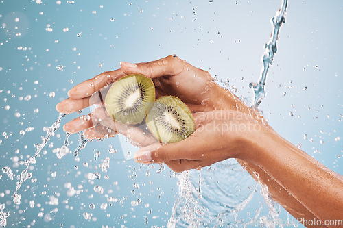 Image of Water splash, hands of woman and kiwi in studio on a blue background. Cleaning, hygiene and female model washing fruits for healthy diet, nutrition and vitamin c for skincare, beauty and wellness.