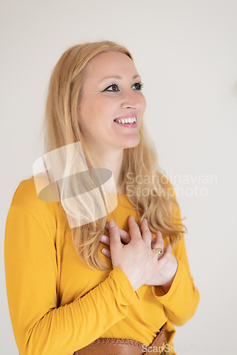 Image of Portrait of cheerful confident beautiful woman with long blond hair, wearing casual clothes, standing in relaxed pose with hands on chest, breathing deeply, doing breathing exercise