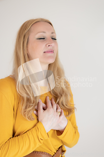 Image of Portrait of cheerful confident beautiful woman with long blond hair, wearing casual clothes, standing in relaxed pose with hands on chest, breathing deeply, doing breathing exercise