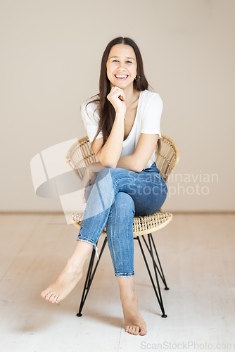 Image of Portrait of confident beautiful woman with long brown hair, wearing casual clothes, sitting on chair in tight jeans and white t-shirt, studio background