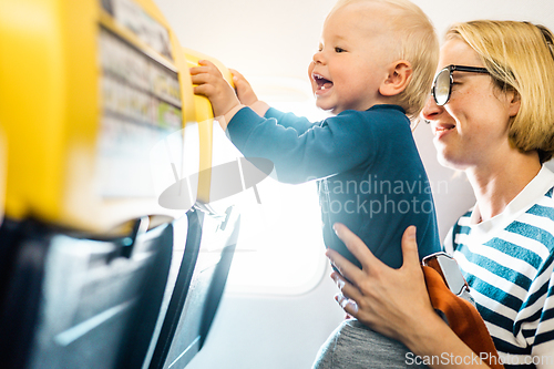 Image of Mom and child flying by plane. Mother holding and playing with her infant baby boy child in her lap during economy comercial flight. Concept photo of air travel with baby. Real people.