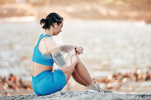 Image of Fitness, smartwatch time and woman at beach on outdoor technology for exercise results, progress and development check. Runner, sports and athlete with smart watch, cellphone and listening to music