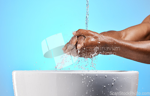 Image of Clean, water and man washing his hands for hygiene, to stop germs and prevent bacteria in a studio. Wellness, health and closeup of a guy cleaning his hand by a basin isolated by a blue background.