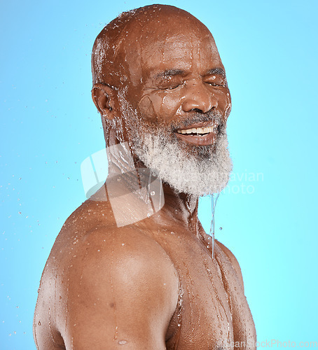 Image of Water splash, skincare and face of senior black man in studio isolated on a blue background. Cleaning, hygiene and retired elderly male from Nigeria bathing or washing for wellness and healthy skin.