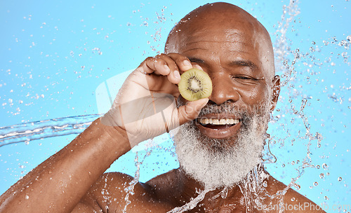 Image of Skincare, kiwi and senior man in studio for beauty, water splash and wellness on blue background mockup. Beauty splash, fruit and water with elderly man cleaning, happy and relax with nature product