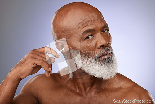 Image of Black man, cleaning ear and cotton bud for hygiene, wellness and wax with face, portrait and purple studio background. Senior male with ears, cleaner and self care for earwax , remove and stick