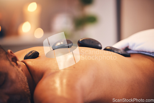 Image of Massage, hot stone and relax with a man in a spa, lying on a table or bed for physical therapy at a luxury resort. Wellness, rock and zen with a male customer relaxing in a health center for rest