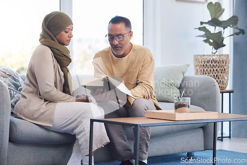 Image of Worship, muslim and couple reading the quran for gratitude on sofa in their living room together. Islam, retirement and senior man and woman with a hijab studying the islamic religion during ramadan.