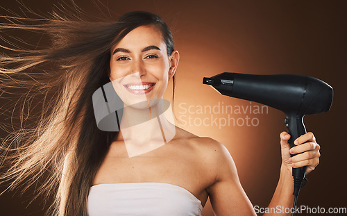 Image of Beauty, hair and hairdryer with a model woman in studio on a brown background for blowdrying or treatment. Portrait, haircare and style with an attractive young female drying or styling her locks