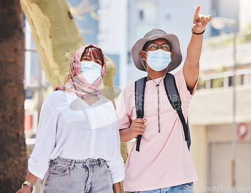 Image of Covid, travel and tourism with a muslim couple pointing while sightseeing outdoor overseas or abroad. Tourist, mask and honeymoon with an islamic man and woman traveling in the corona virus pandemic