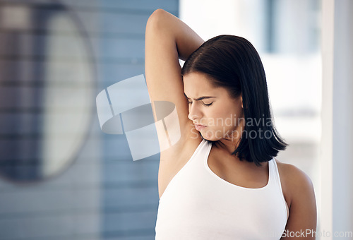 Image of Woman smelling her armpit in a bathroom at her home before a shower for hygiene, wellness and health. Girl checking her underarm before washing and spraying deodorant or perfume at her modern house.