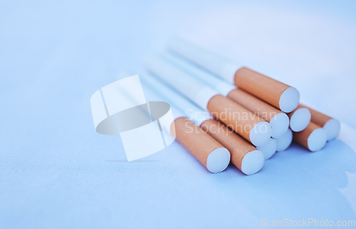 Image of Cigarette, cancer and smoke with a tobacco product on the ground against a blue background to promote awareness. Smoking, toxic and addiction with cigarettes in a pile or stack on the floor