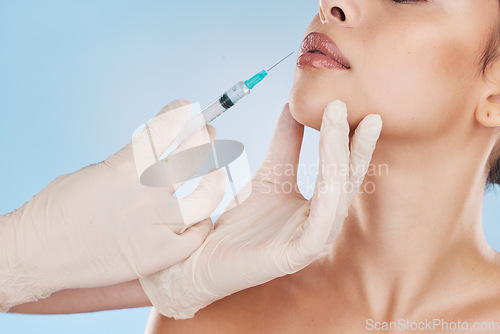 Image of Lips, plastic surgery and filler with woman getting an injection with a syringe from the hands of a surgeon in gloves. Mouth, face and needle for beauty treatment in studio on a blue background.