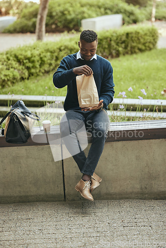 Image of Black business man on a lunch break in the city, sitting and eating a meal or sandwich in a brown paper bag. Hungry worker relaxing with a tasty snack, food on the go for a professional entrepreneur
