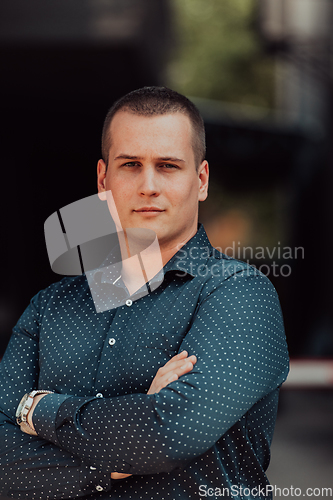 Image of A successful young businessman in a shirt, with crossed arms, poses outdoors, confident expression on his face.